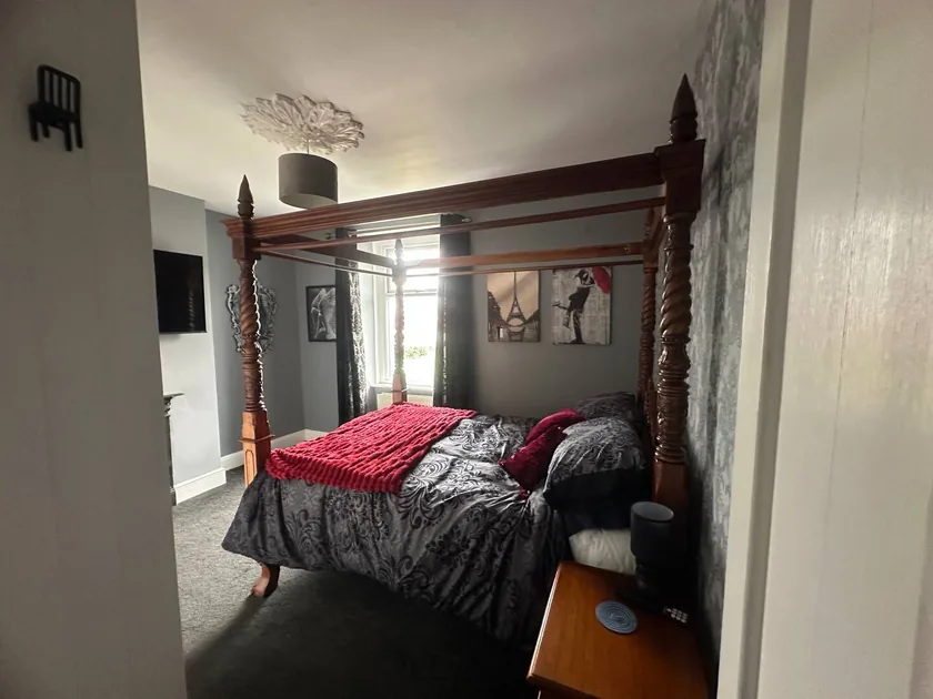 Wooden four-poster bed with patterned bedding and a red throw.