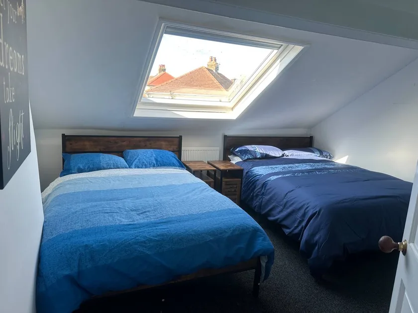 Two beds with blue bedding beneath a sloping ceiling and roof window.