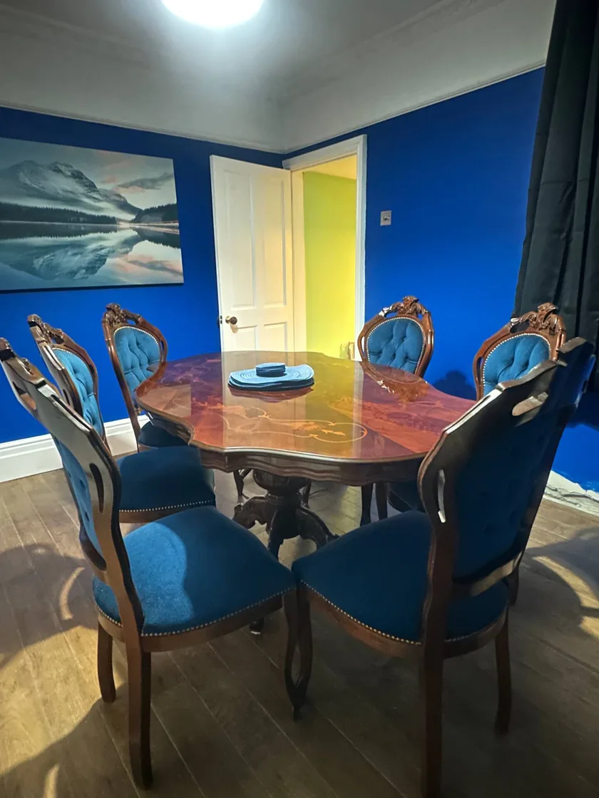 Wooden dining table and blue upholstered chairs in a blue-walled room.