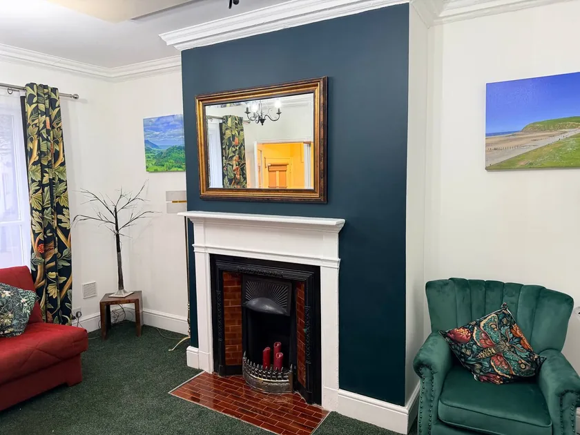 Sitting room with a green armchair, red sofa, decorative fireplace and framed mirror.
