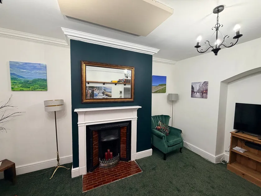 Sitting room with a decorative fireplace, green armchair and television on a wooden stand.