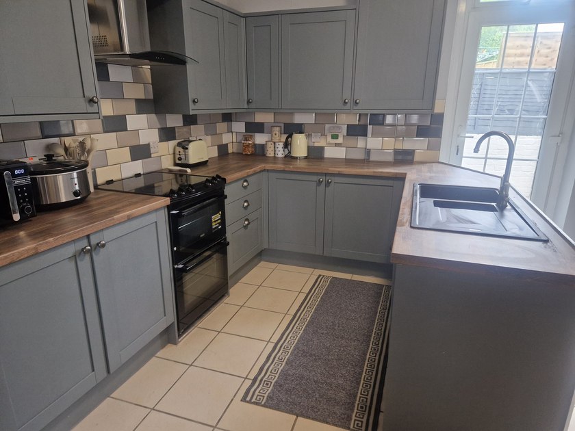 Kitchen with grey cabinets, wood-effect worktops, cooker and sink beside the window.