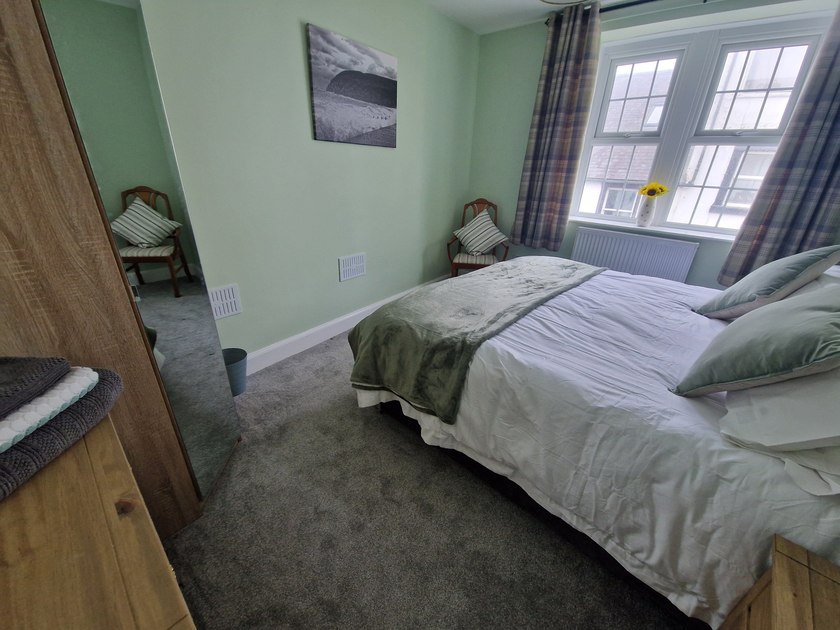 Double bed with pale green cushions and throw beside a large window, with a mirrored wardrobe to the left.