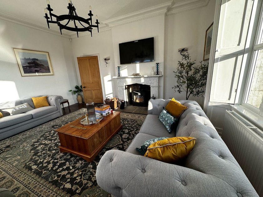 Grey sofas and a wooden chest coffee table face a wood-burning stove beneath a wall-mounted television.