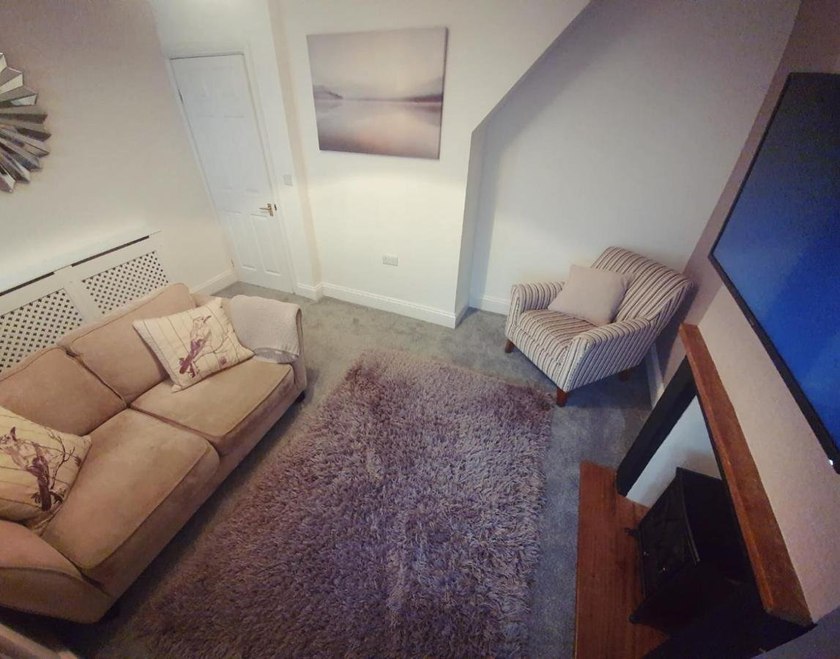 Sitting room with a sofa, striped armchair, rug, television and fireplace surround.